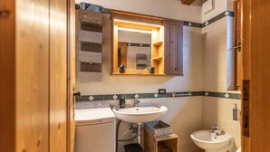 A bathroom with a sink, mirror, and bidet. There is a wooden cabinet above the sink and a small step stool next to it. - Casa Noce, quiet and surrounded by nature (Cortina d´Ampezzo)