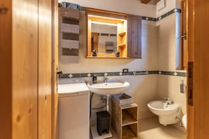 Ein Badezimmer mit Waschbecken, Spiegel und Bidet. Über dem Waschbecken befindet sich ein Holzschrank und daneben ein kleiner Trittschemel.