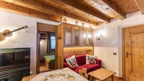 A cozy room with a wooden ceiling, a piano, a red sofa with decorative pillows, and a wooden table. - Casa Noce, quiet and surrounded by nature (Cortina d´Ampezzo)
