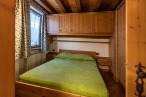 A small, cozy room with a single bed, wooden walls, a window with patterned curtains, and a built-in wooden cabinet above the bed. - Casa Noce, quiet and surrounded by nature (Cortina d´Ampezzo)