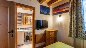 A bedroom with a wooden bed, a television, a dresser, and a bathroom visible through an open door. - Casa Noce, quiet and surrounded by nature (Cortina d´Ampezzo)