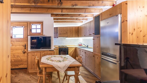 A wooden kitchen with a dining table, wooden cabinets, a stainless steel refrigerator, and a television. - Casa Noce, quiet and surrounded by nature (Cortina d´Ampezzo)