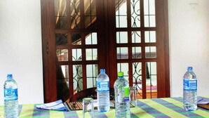 A table with a checkered tablecloth, water bottles, and a chair in front of a wooden door with glass panels. - Keerthi Homestay (Sigiriya)