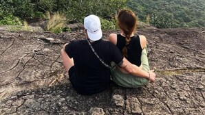 Two people sitting on a rocky outcrop overlooking a forested valley with a prominent rock formation in the distance. - Keerthi Homestay (Sigiriya)