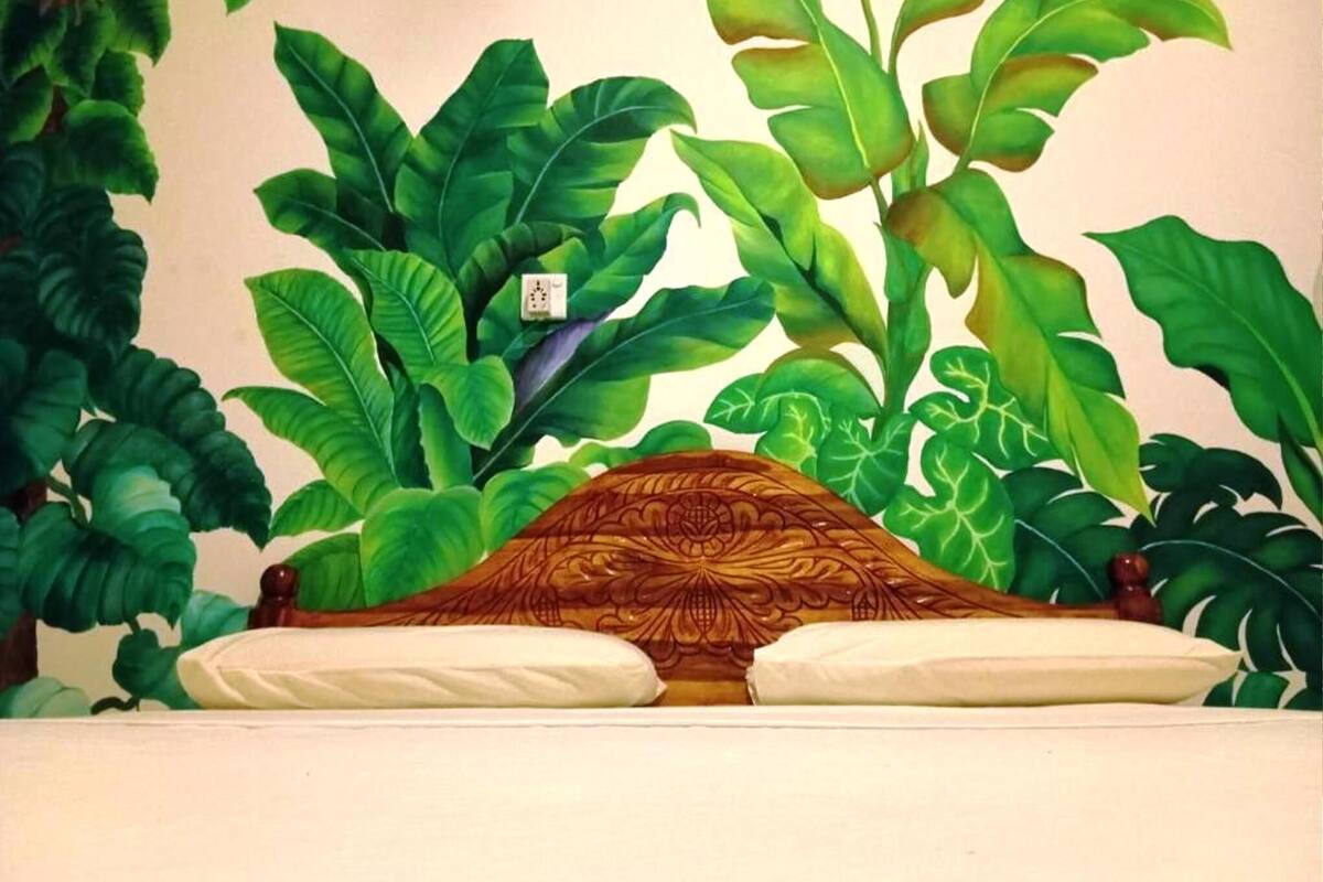 A bed with a wooden headboard and white pillows, surrounded by large green plants.