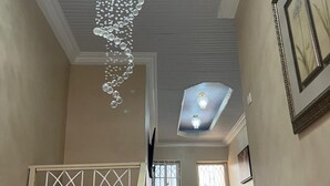 Een trap met een decoratieve kroonluchter, een lijst met een afbeelding en een plafondlamp.