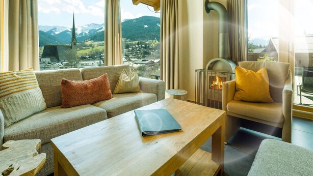 A cozy living room with a sofa, armchair, and table, a fireplace, and a scenic mountain view. - eder.VIEW (Maria Alm am Steinernen Meer)