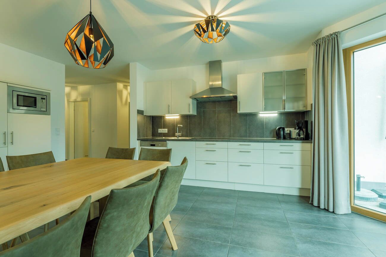 Een moderne keuken met een eethoek, met een houten tafel, stoelen en hanglampen.