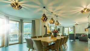 A spacious dining area with a wooden table and chairs, a chandelier, and large windows with a view of the outdoors. - eder.VIEW (Maria Alm am Steinernen Meer)