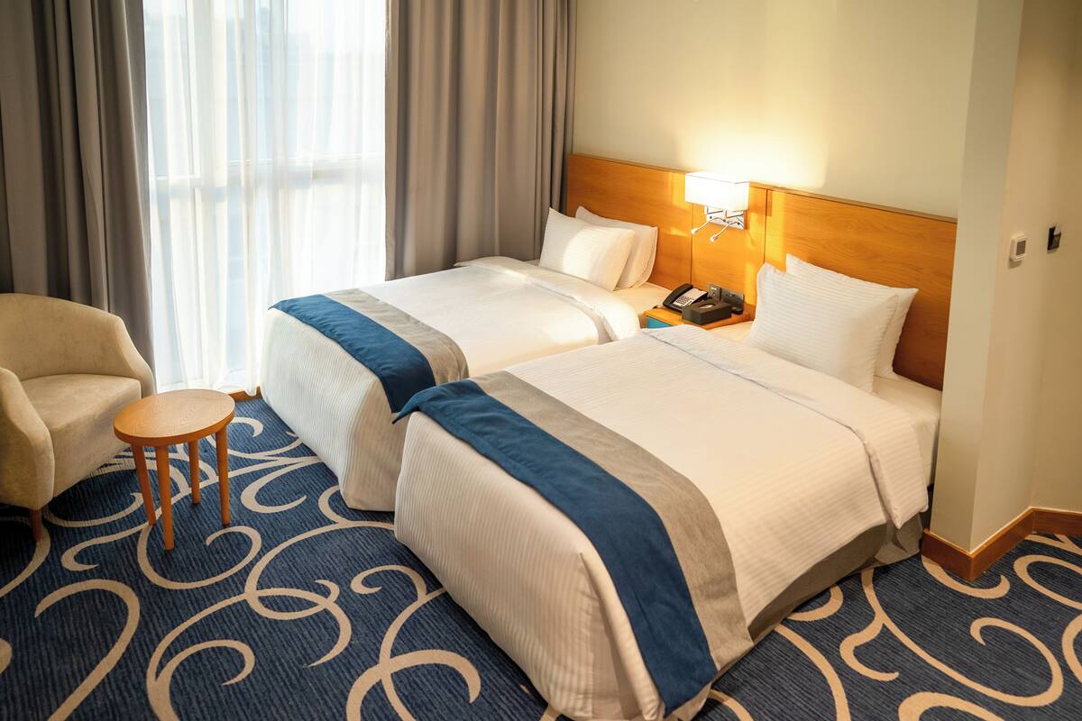 A hotel room with two beds, a chair, a small table, and a nightstand with a phone.