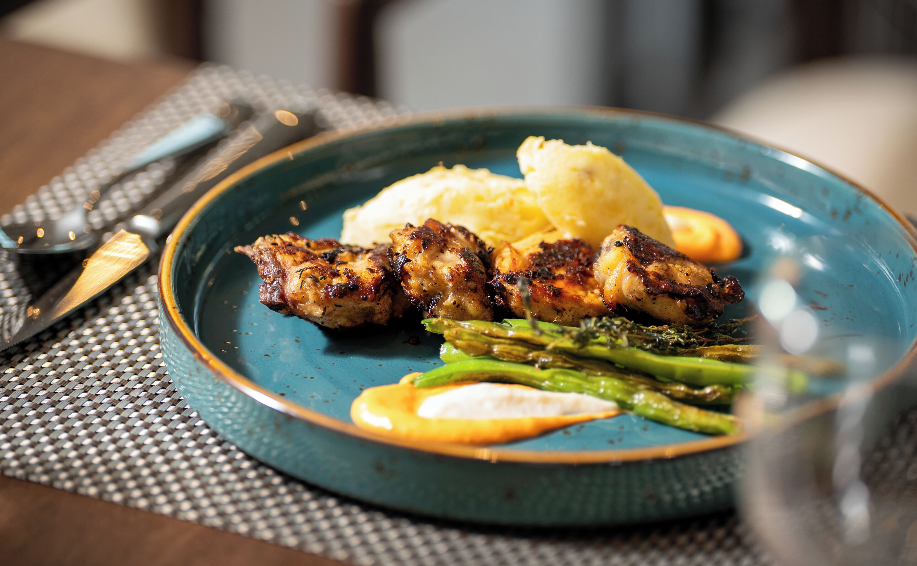 Une assiette de poulet grillé, de purée de pommes de terre et d’asperges, le tout servi dans une assiette bleue.