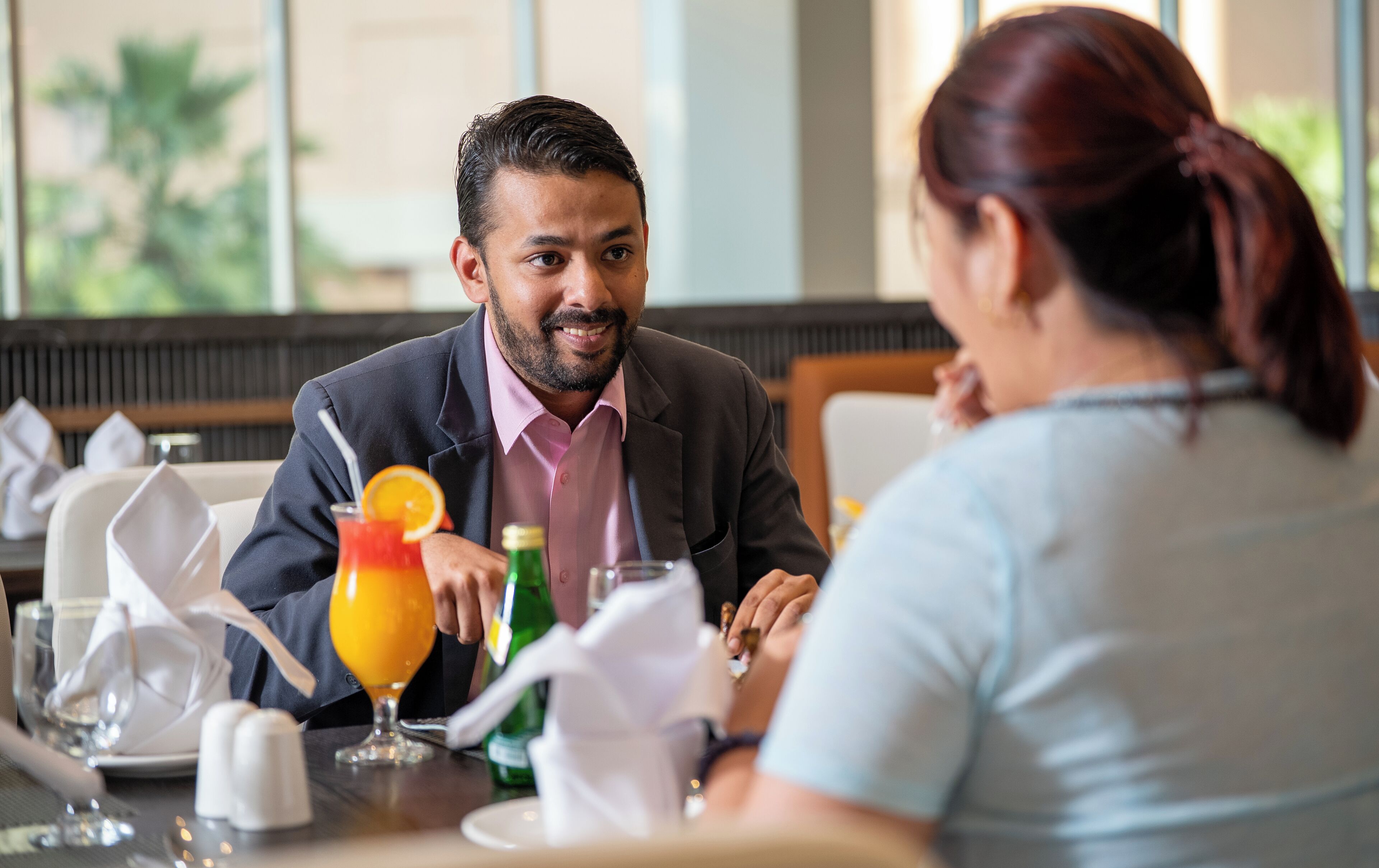 Comedor con una mesa preparada para dos personas, que incluye un vaso de jugo de naranja, una botella de agua y una servilleta.