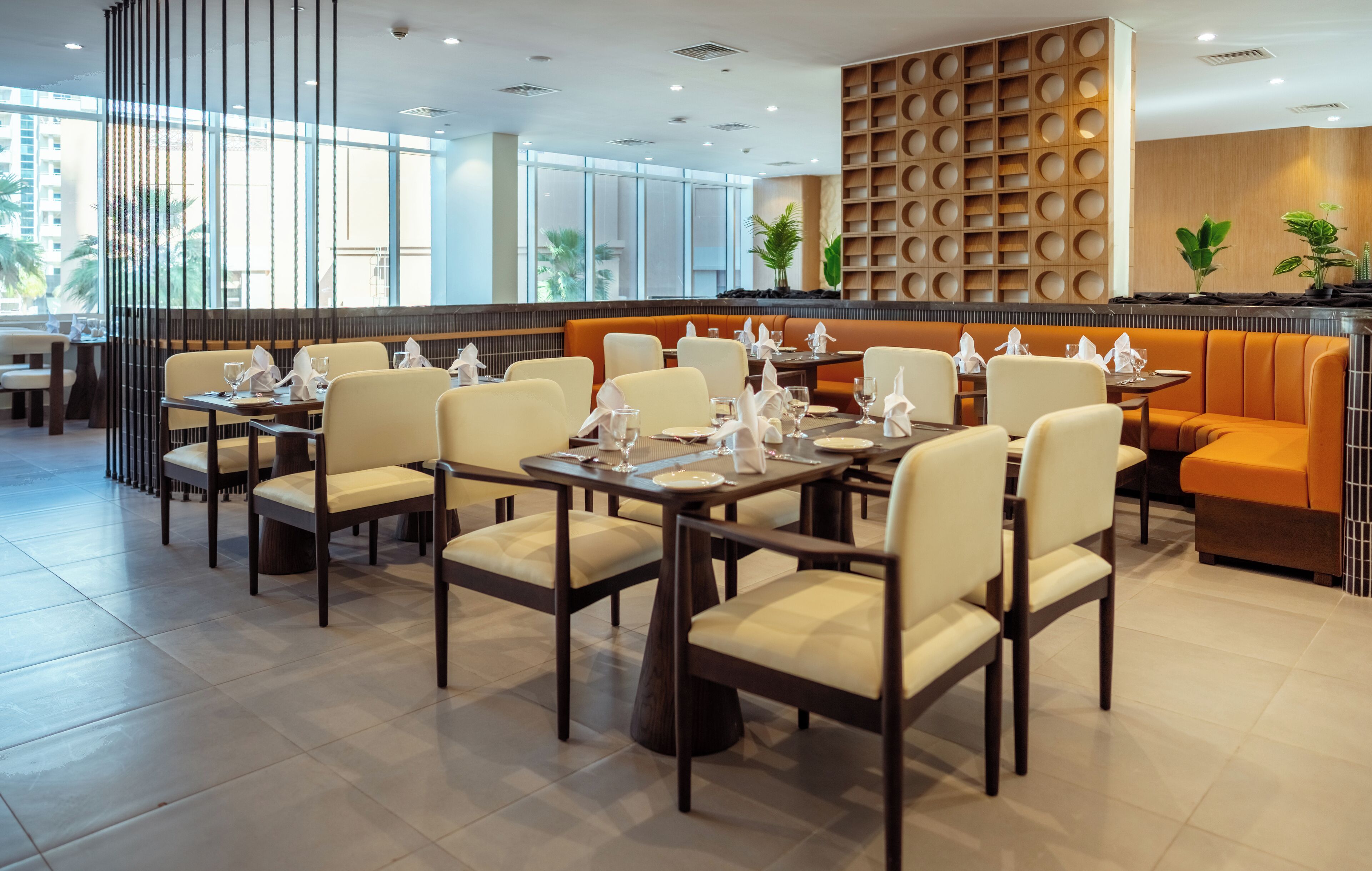 A modern dining area with tables and chairs, a wooden accent wall, and large windows.