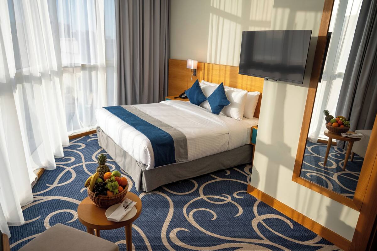 A hotel room with a large bed, a television, a fruit basket, and a small table with a napkin and fork.