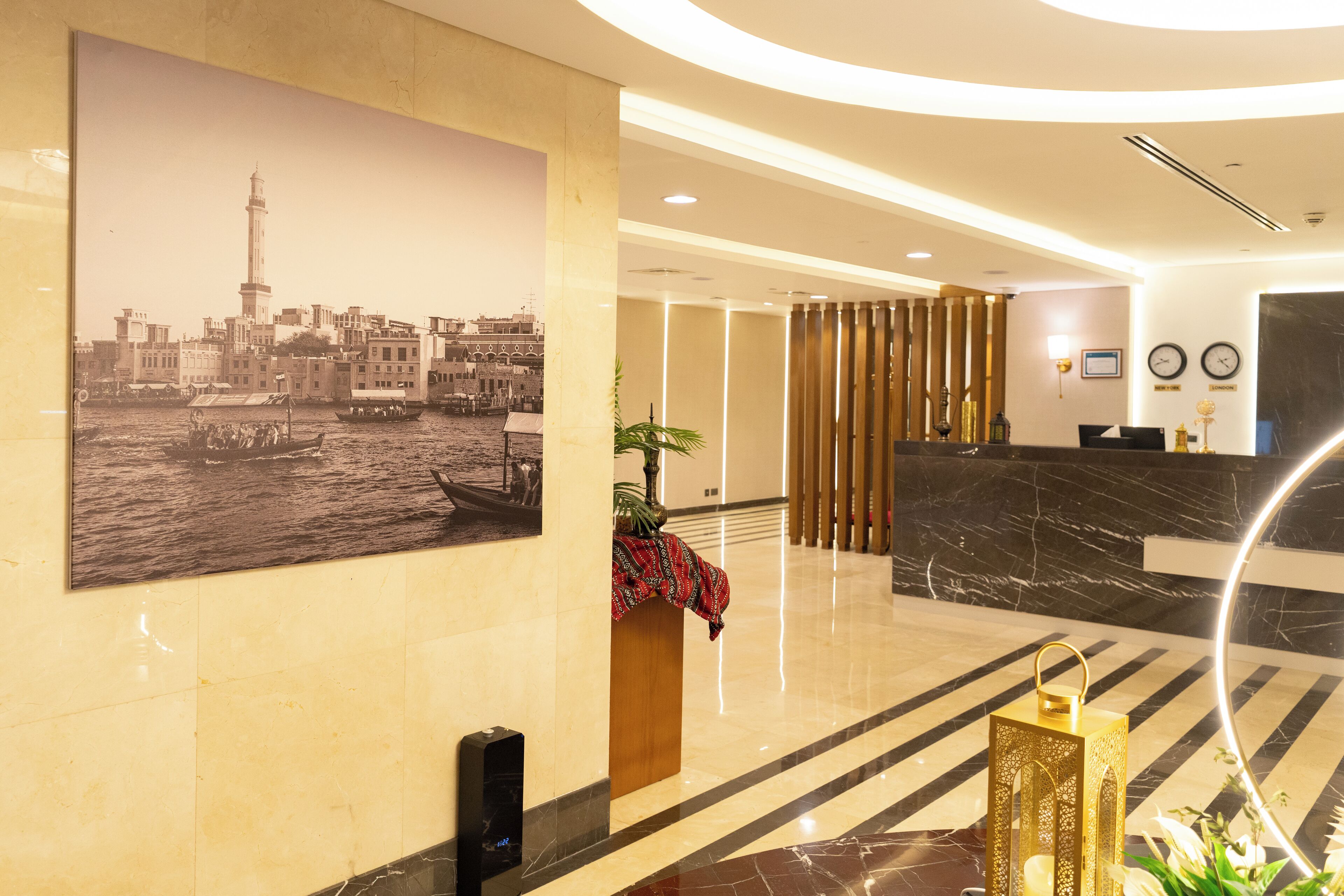 Un vestíbulo de hotel con una recepción, una fotografía de gran formato del paisaje urbano, una planta y un farol decorativo.
