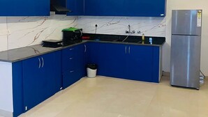 A modern kitchen with blue cabinets, a marble backsplash, and a stainless steel refrigerator. - Greek House By Housiify (Gurugram)