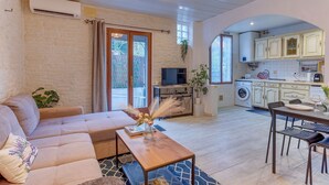 Een woonkamer met een bank, salontafel en televisie, grenzend aan een keuken met kasten en apparatuur.