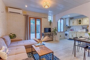 Ein Wohnzimmer mit Sofa, Couchtisch und Fernseher, verbunden mit einer Küche mit Schränken und Geräten.