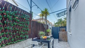 Een klein terras buiten met een tafel en stoelen, een decoratieve plantenwand en uitzicht op een woonwijk.