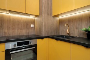 A modern kitchen with yellow cabinets, a black countertop, stainless steel appliances, and a built-in oven. - Modern Apartment | Balcony, Parking, Close to Expo (Łódź)
