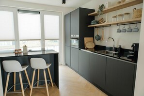 A modern kitchen with a central island, two bar stools, and a built-in oven. - A large detached Watervilla with Sauna and view of the outer harbour (Heeg)