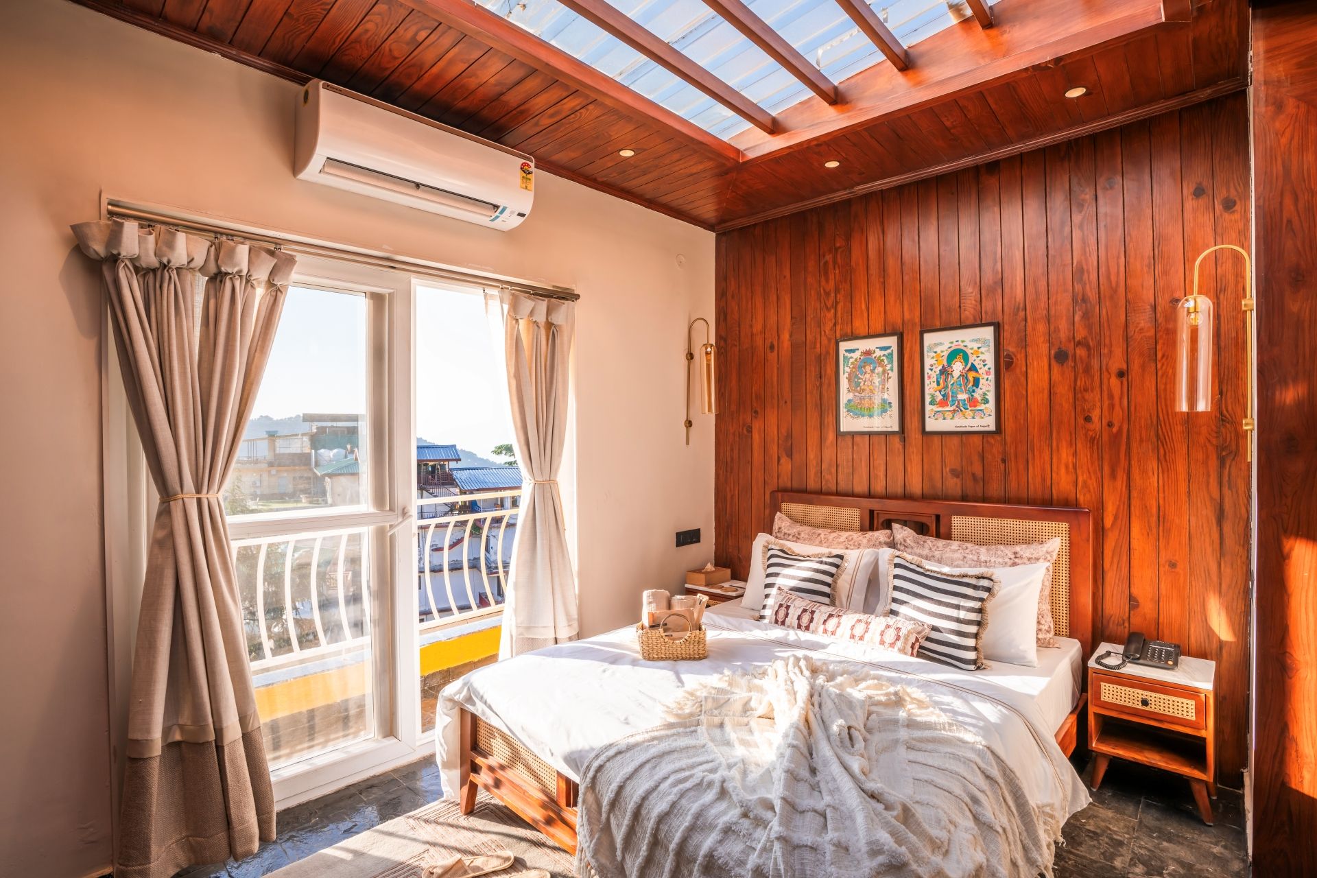 A bedroom with a wooden ceiling, a bed with multiple pillows, a bedside table with a lamp, and a window with curtains.