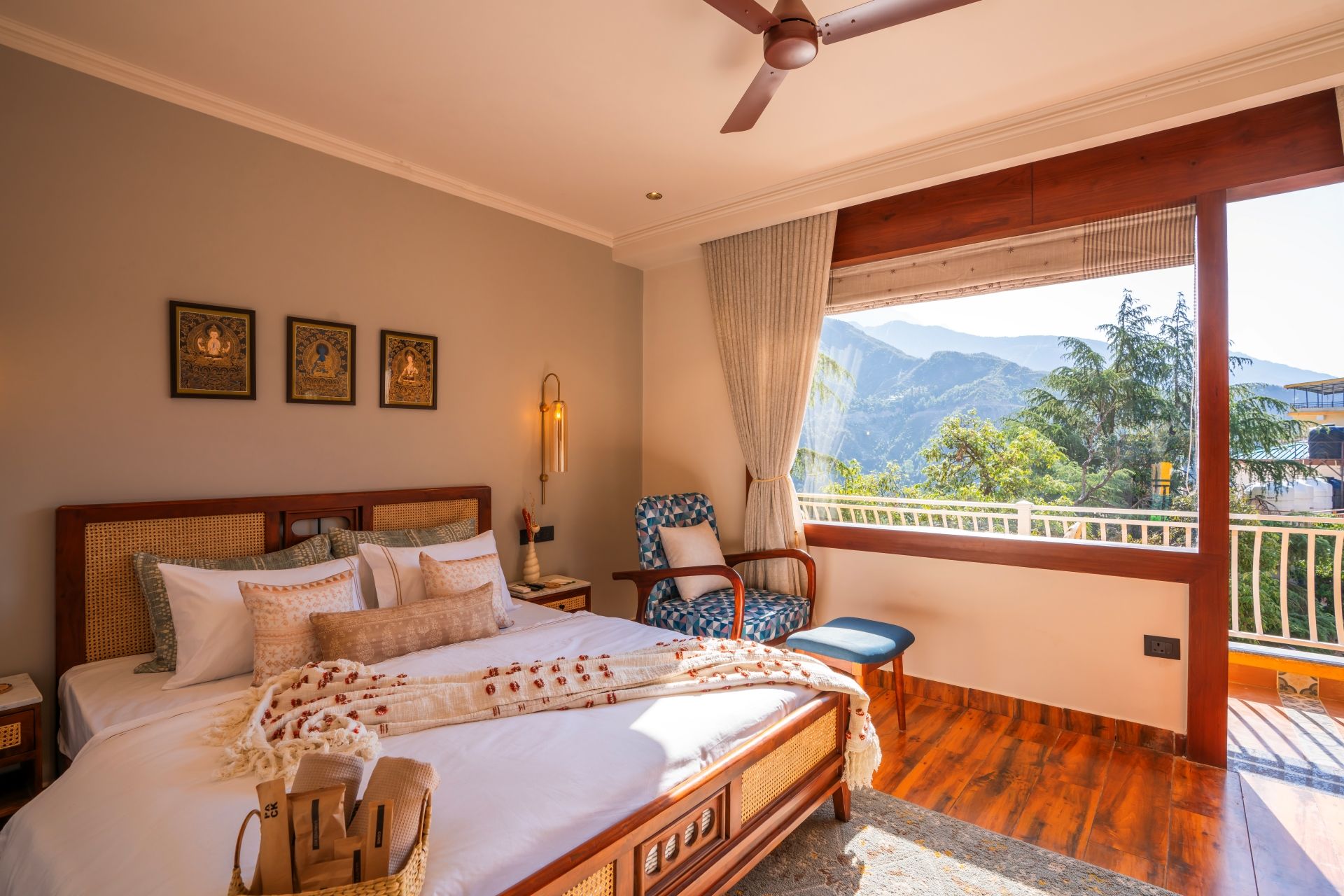 A bedroom with a bed, a chair, a nightstand, a wall-mounted lamp, and a view of mountains through a window.