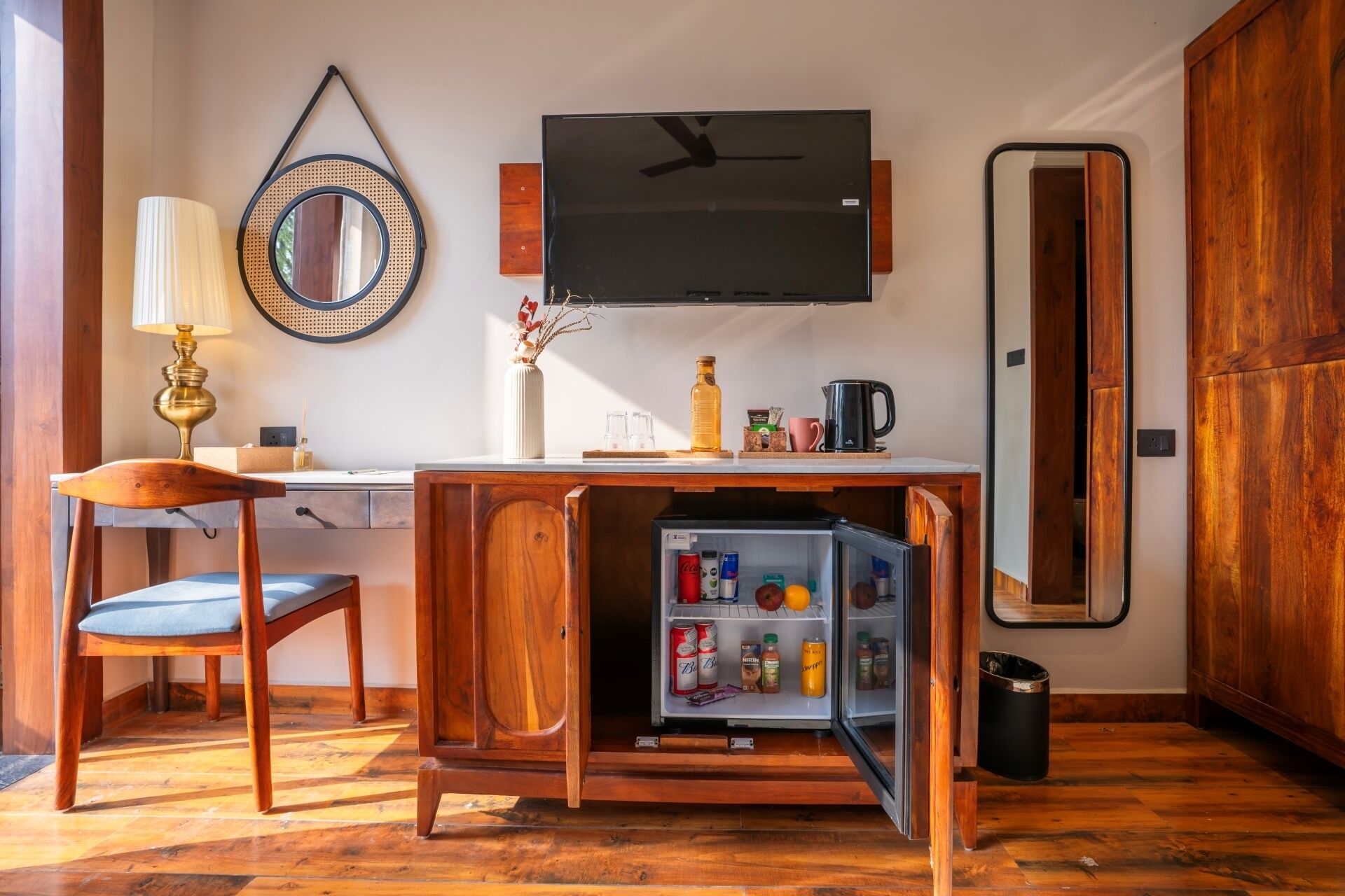 A compact living space with a wooden desk, a chair, a television, a mirror, and a small refrigerator.