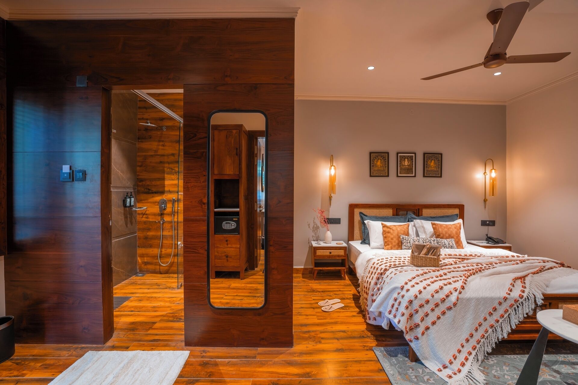 Une chambre moderne avec un plancher en bois, un grand miroir, un lit avec de nombreux oreillers, une table de chevet et un ventilateur de plafond.