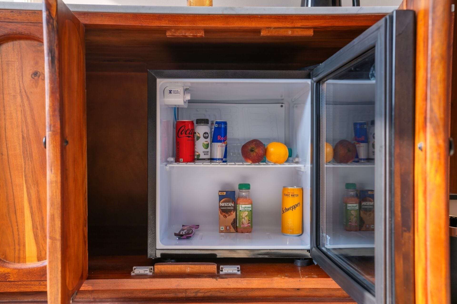 A compact refrigerator with a wooden exterior, containing various beverages and fruits.