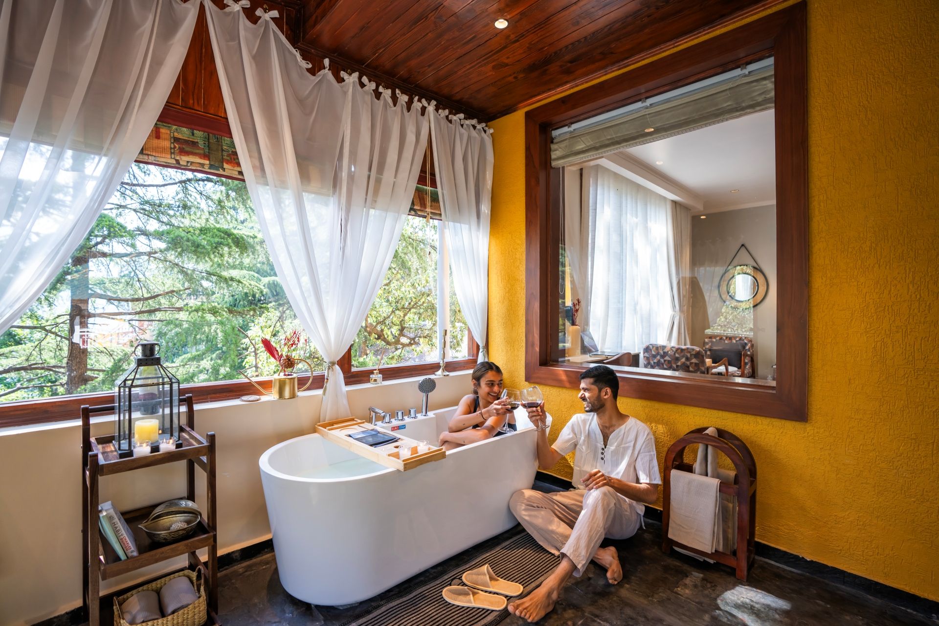 A bathroom with a bathtub, a wooden shelf with toiletries, and a window with curtains.