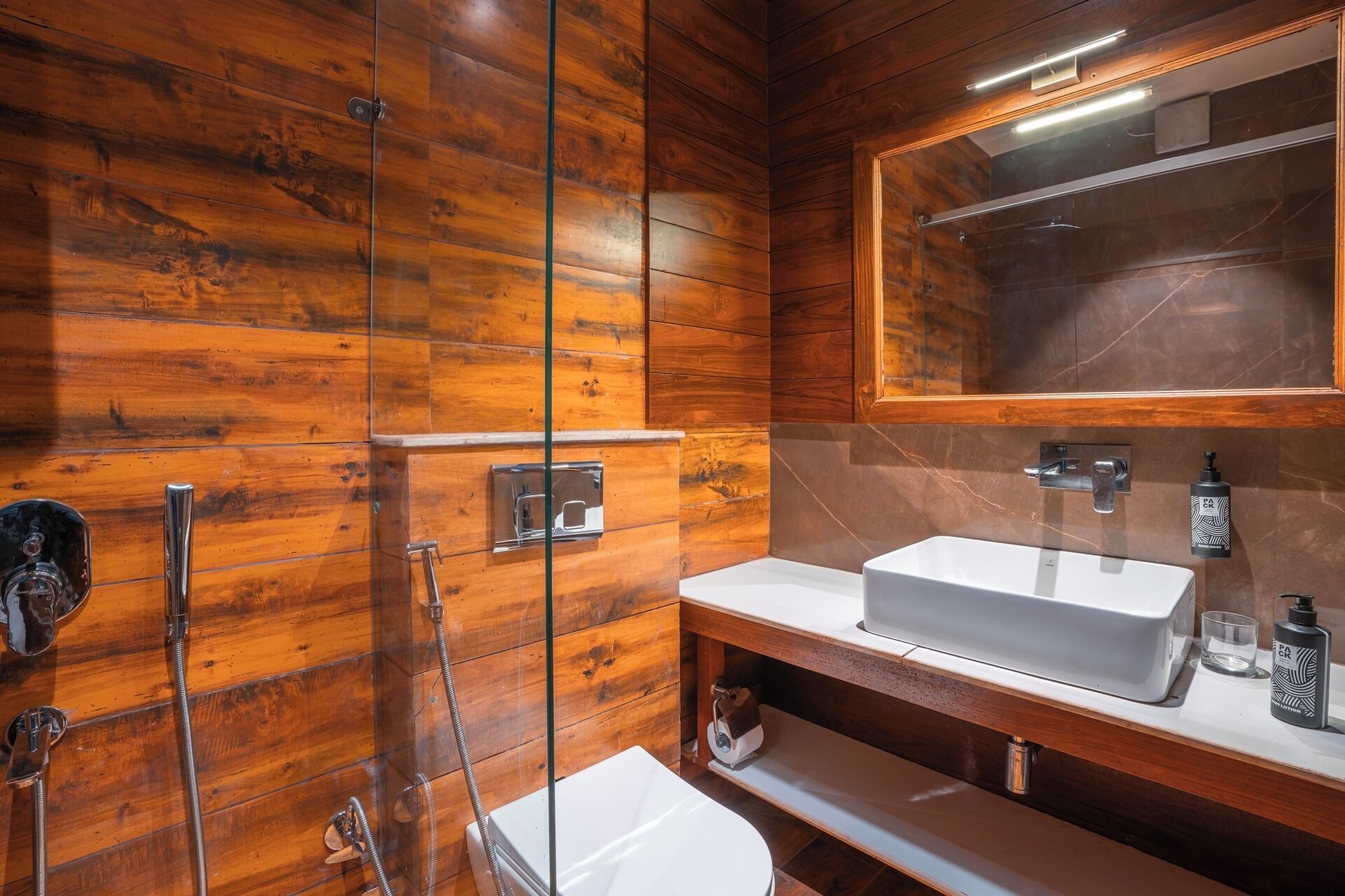 Un baño con paredes de madera, un lavamanos blanco, un espejo y una ducha.