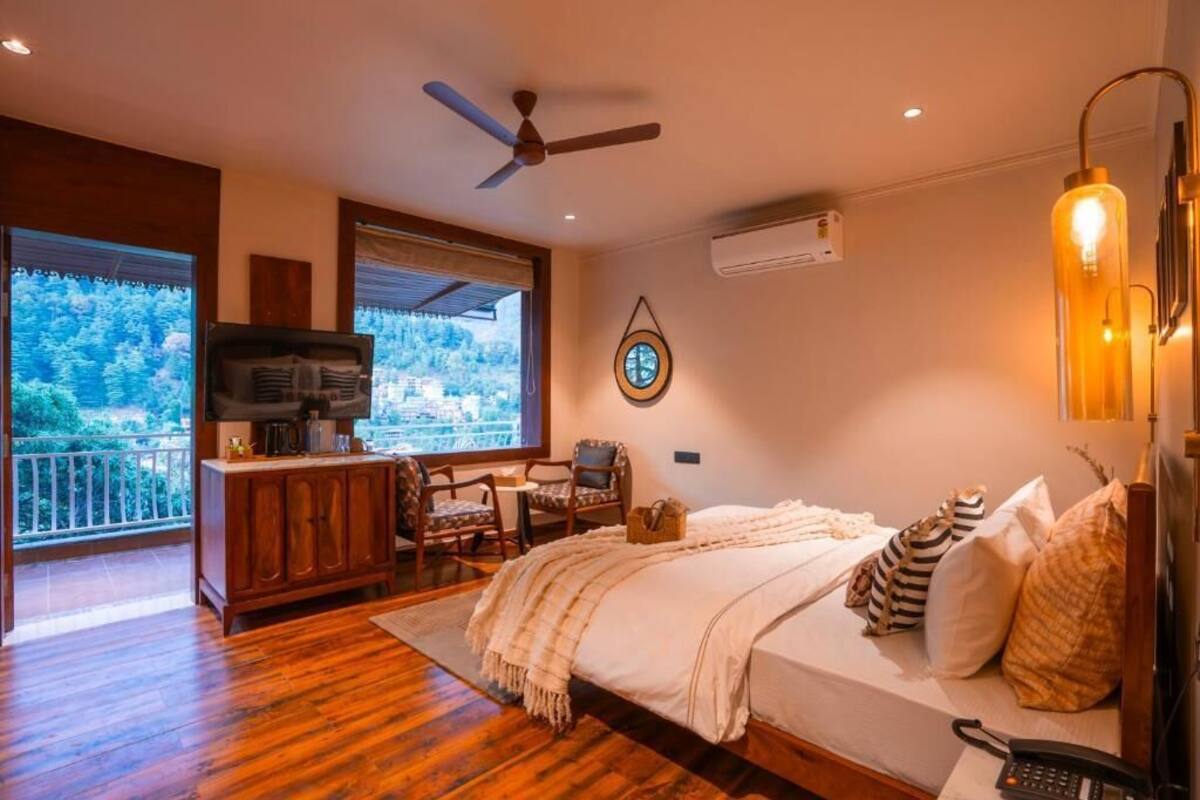 Ein Schlafzimmer mit Bett, Schreibtisch, Stuhl, Fernseher und Blick ins Freie.