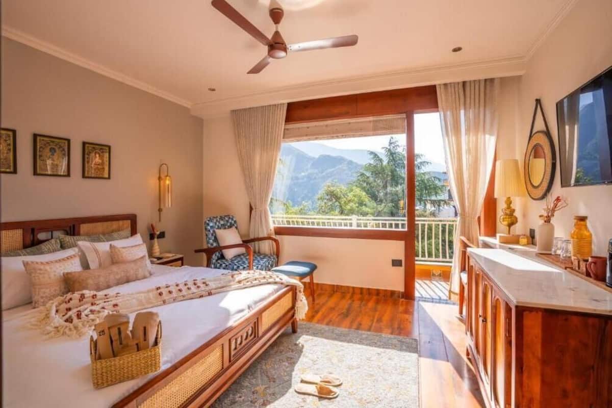 Ein Schlafzimmer mit Bett, Schreibtisch, Stuhl und einem Balkon mit Bergblick.