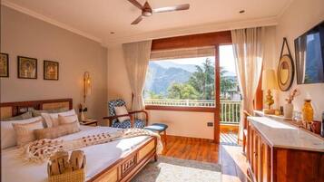 A bedroom with a bed, a desk, a chair, and a balcony with a view of mountains.