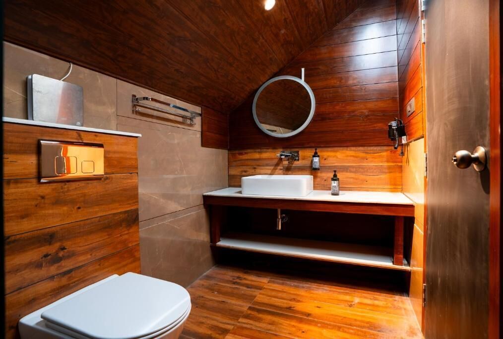 A wooden-paneled bathroom with a white toilet, a sink with a mirror, and a shelf with toiletries.