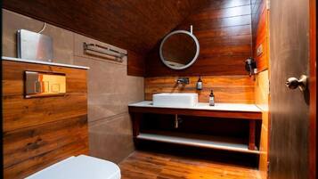 A wooden-paneled bathroom with a white toilet, a sink with a mirror, and a shelf with toiletries.