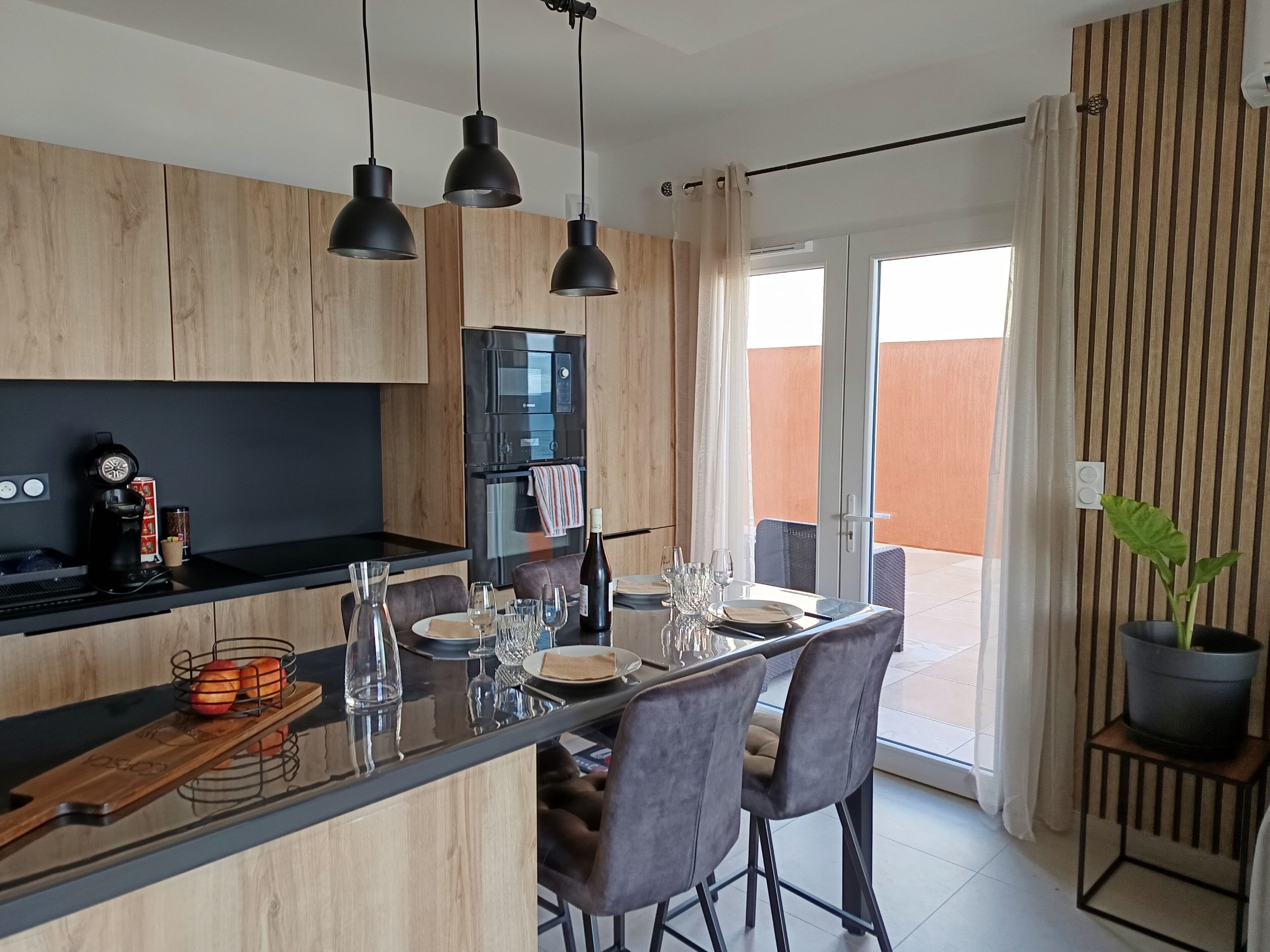 Une cuisine moderne avec des meubles en bois, un plan de travail noir et un coin repas comprenant une table et des chaises.
