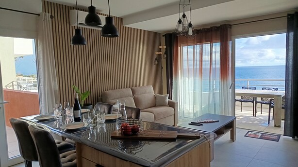 Una sala de estar moderna con una isla grande, un sofá y vista al mar.