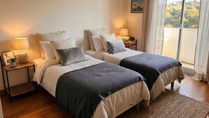 Une chambre avec deux lits, des lampes de chevet, une vue sur les arbres par la fenêtre et un tableau encadré au mur.