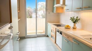 Une cuisine moderne dotée d’une porte-fenêtre coulissante donnant sur un balcon, d’un évier et d’une cuisinière.