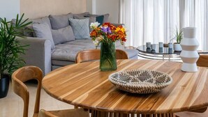 Uma sala de estar moderna com uma mesa de jantar de madeira, sofá cinza e uma janela grande com cortinas.
