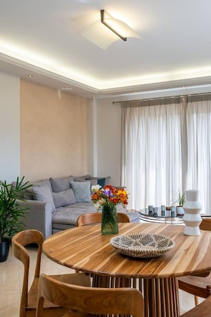 Un salon moderne avec une table à manger en bois, un canapé gris et une grande fenêtre agrémentée de rideaux.