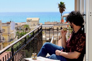 Un balcón con vista al mar, una persona sentada y una taza de café.