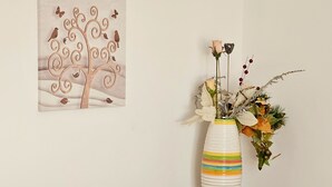 A hotel room with a bed, a wooden nightstand, a vase with flowers, and a painting on the wall.