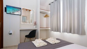 Habitación de hotel con cama, escritorio, silla, televisor y ventana con cortinas.
