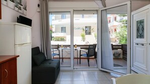 Una habitación con puerta corrediza de vidrio que da a un balcón con mesa y sillas, un sofá y un armario blanco.