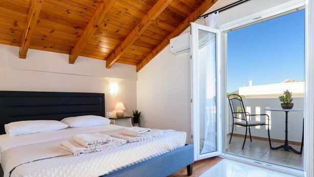 Un dormitorio con una cama, una mesita de noche, una lámpara y vistas a un balcón exterior con una silla y una mesa.