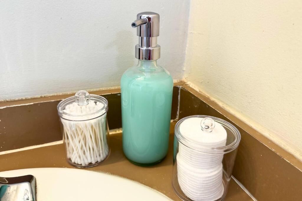 A bathroom counter with a soap dispenser, a container of cotton swabs, and a container of cotton pads.