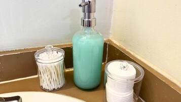 A bathroom counter with a soap dispenser, a container of cotton swabs, and a container of cotton pads.